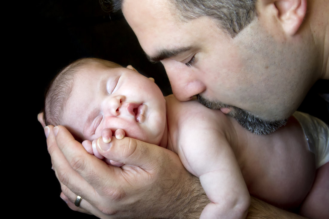 dad kissing newborn on back while holding in his hands