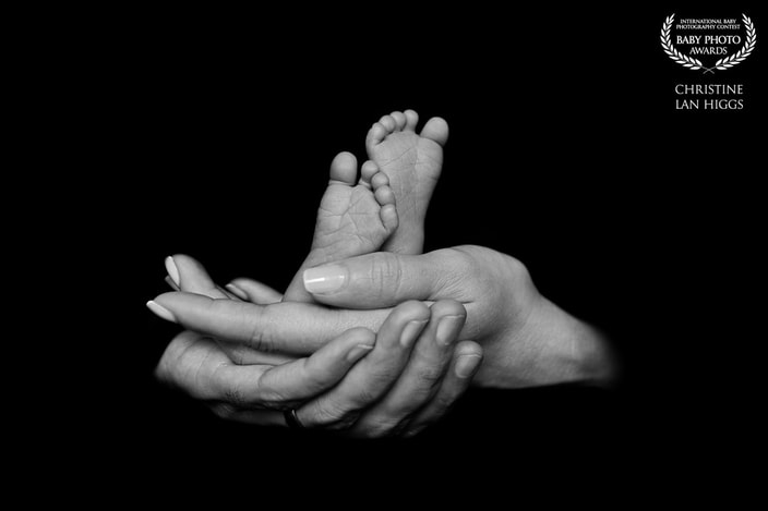 black and white of two adult hands holding infant feet