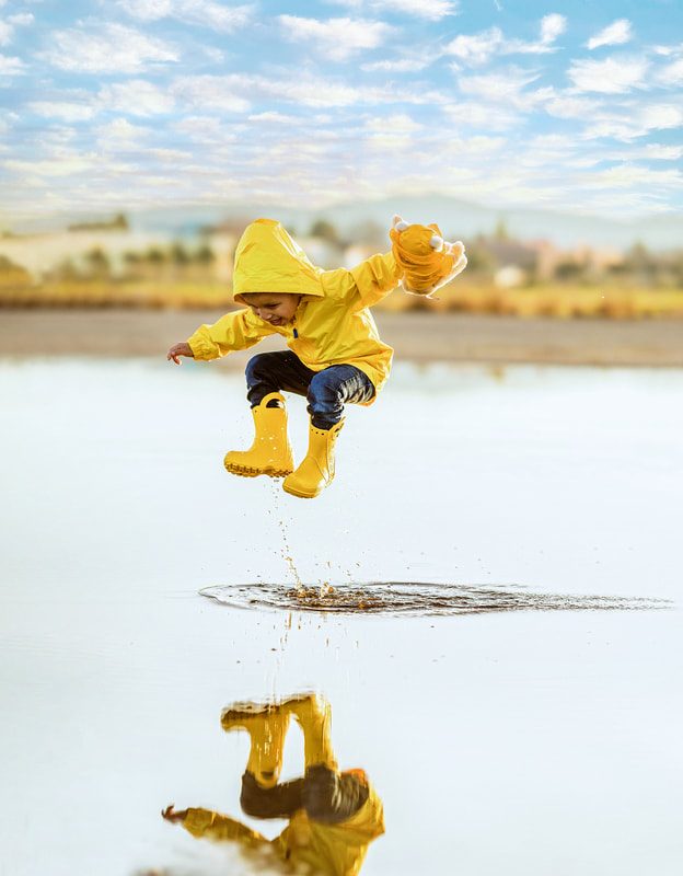 boy in yellow raincoat and boots jumping in puddle