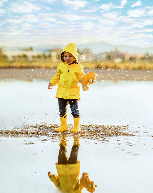 boy in yellow coat and boots landing in puddle