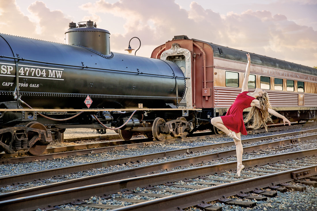 teenager in red dress in a ballet pose on train tracks