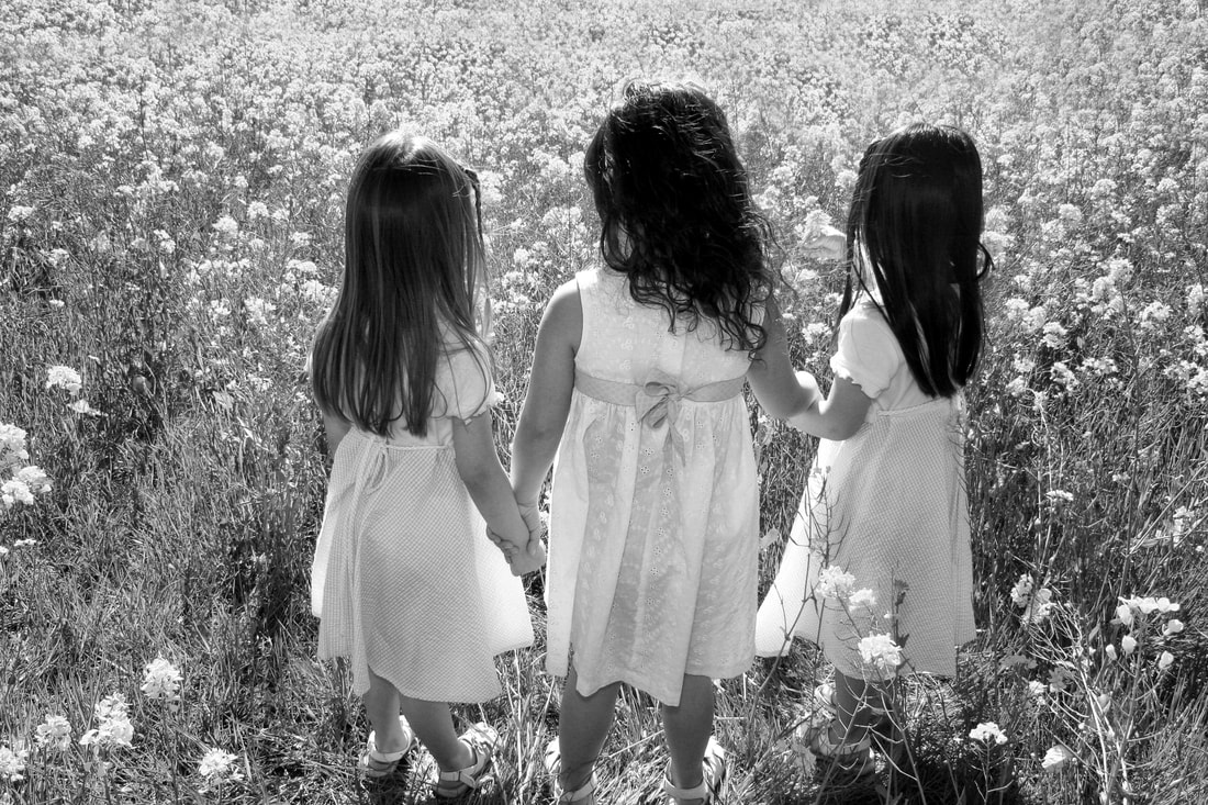 black and white of three young girls in flower field holding hands