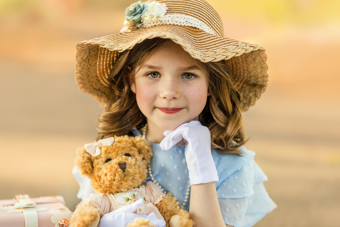 young girl in a straw hat holding a bear and wearing white gloves smiling