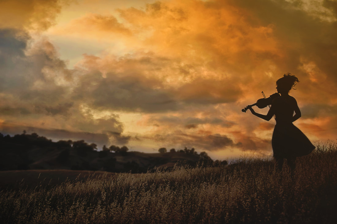 silhouette of woman playing violin in the hills at sunset