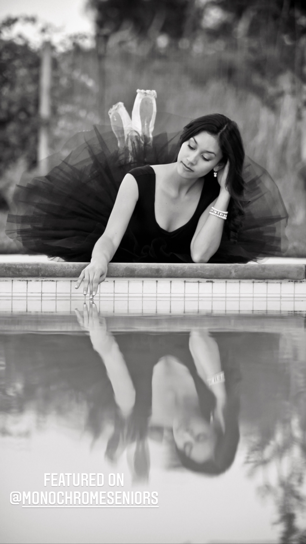 teenage girls with long dark hair in black tutu touching a pool of water with finger