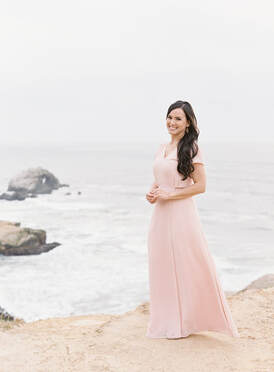 Christine Lan Higgs in pink flowy dress on a cliff by the ocean