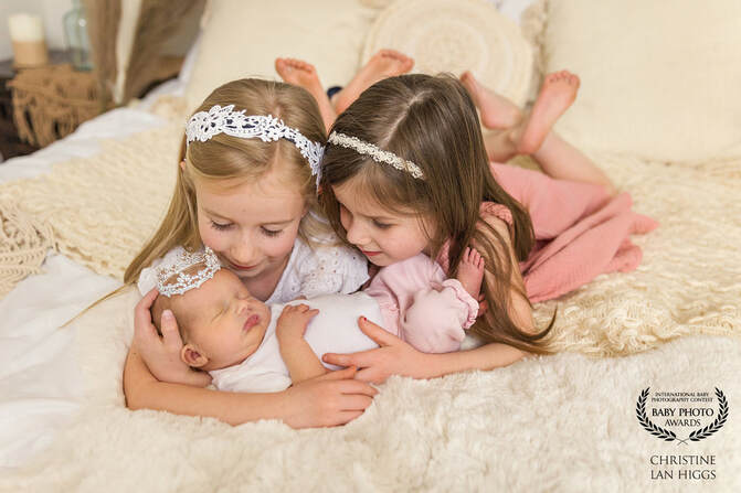two little girls holding their baby sister on a bed