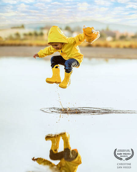 boy in yellow jacket and boots jumping in a puddle