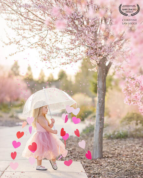 young girl in pink dress holding an umbrella with hearts under a pink blossom tree