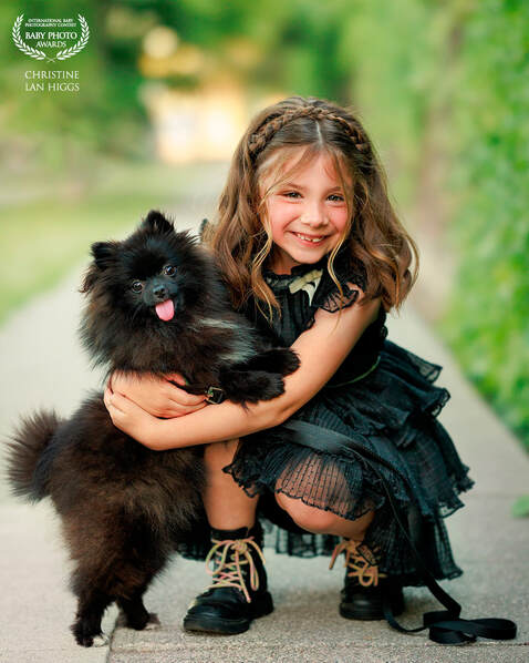 Young girl in black dress hugging little black dog with tongue sticking out.