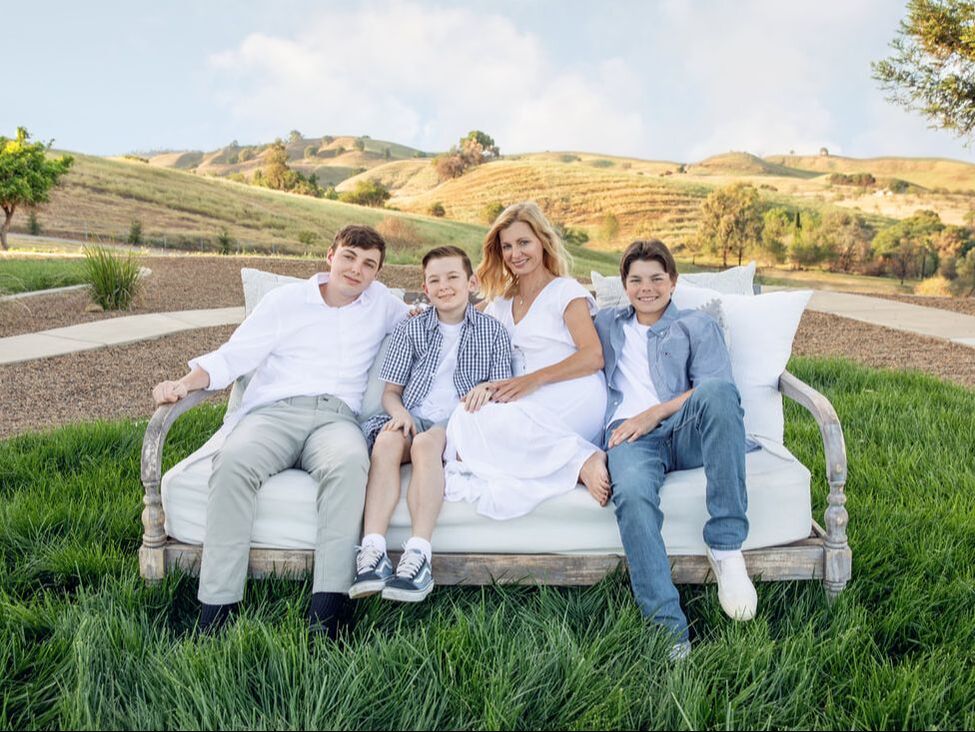 mom in white dress with three sons sitting on a couch on the grass