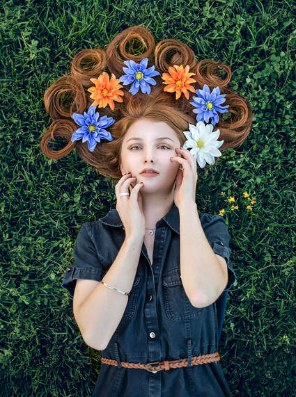 teenage girl with red hair laying on the grass with flowers in her hair