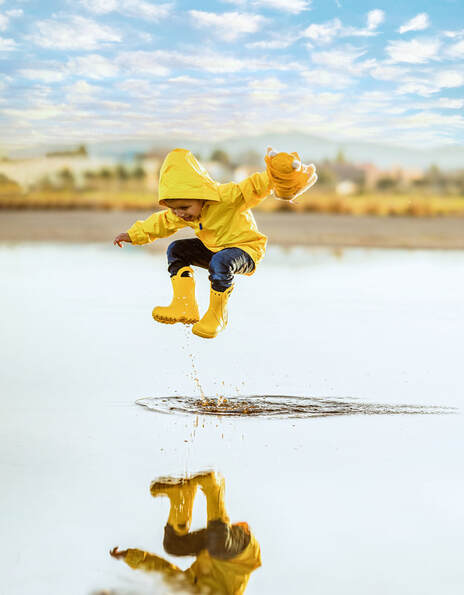 boy in raincoat jumping in a puddle