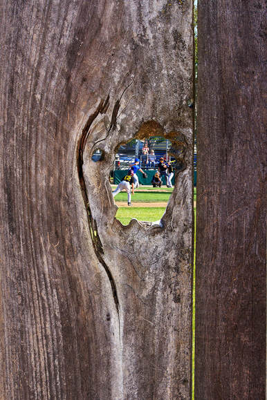 baseball game seen through the hole of a fence