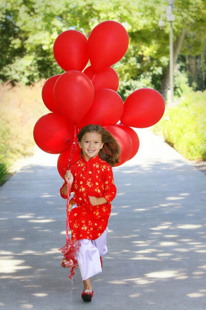 young girl in red Vietnamese dress running with red balloons
