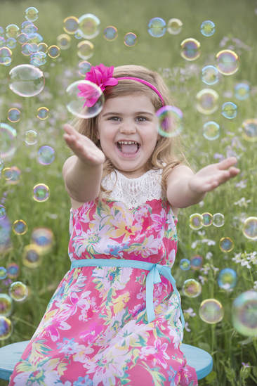 young girl sitting in pink dress with lots of bubbles around her