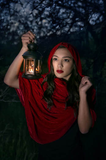 teenager in red hooded cape with lantern walking in the dark