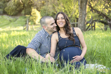 male and pregnant female sitting in the grass laughing