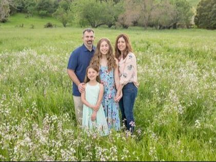mom and dad with two daughters standing in flower field