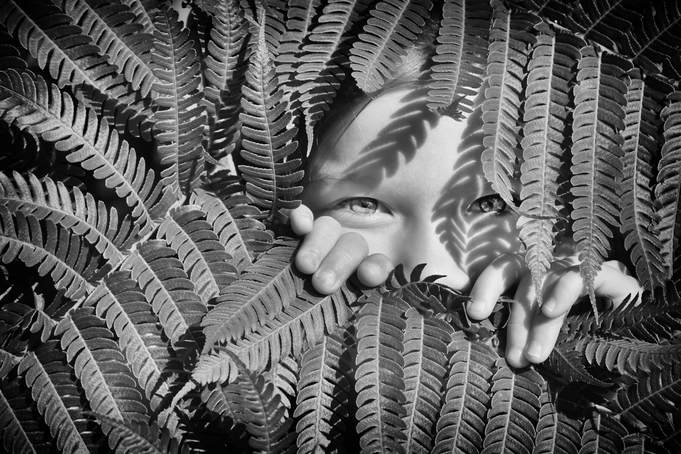 black and white of young girl peaking through a fern