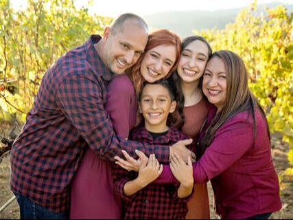 mom and dad with three kids holding each other in a vineyard
