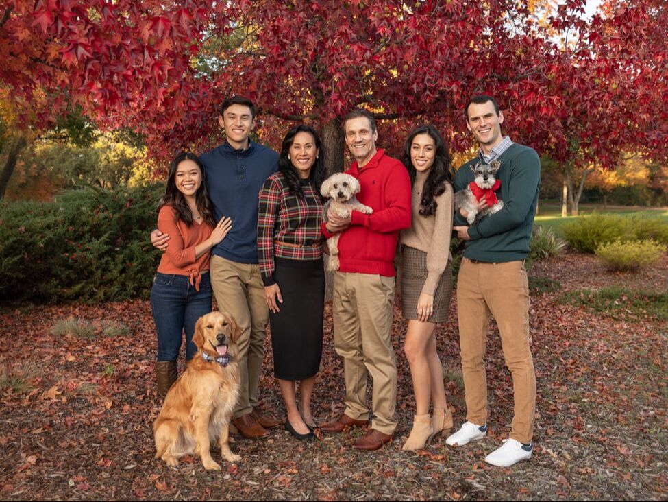 mom and dad with four kids and three dogs standing under fall red tree