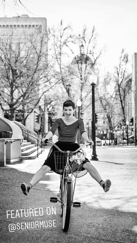 teenage girls with short hair riding bike towards camera with legs up in a black skirt and stripped shirt