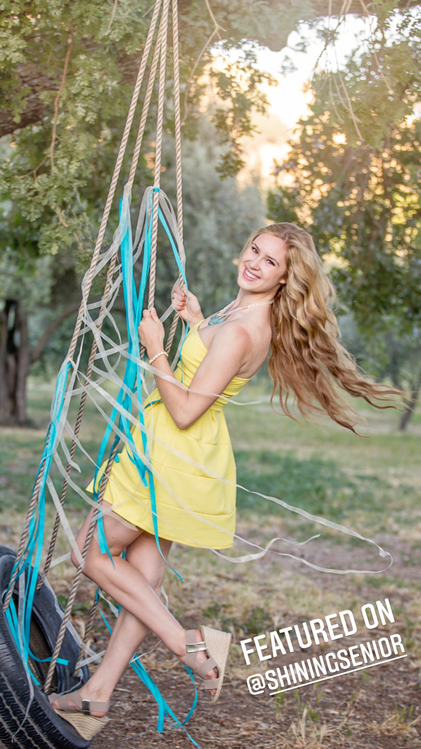 teenage girl with long blonde hair in a yellow dress swinging on a tire swing 