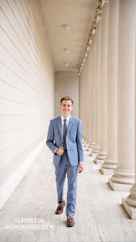 teenage boy in blue suit walking towards the camera next to white columns