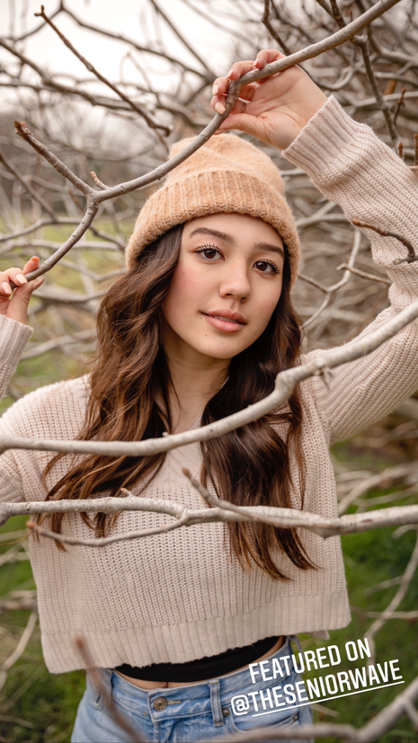 teenage girl with knitted beige hat and sweater looking through dead tree branches