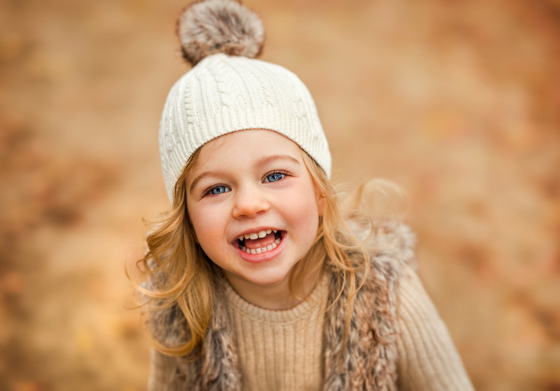 close up of little girl in a knitted white hat smiling big