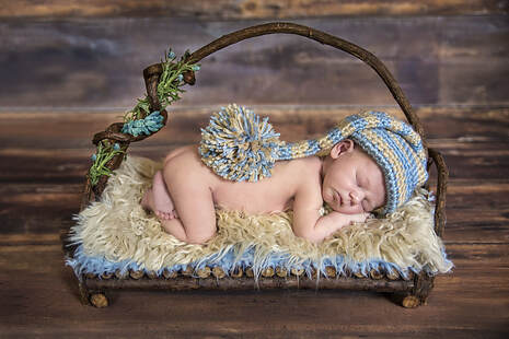 naked newborn baby with knitted hat laying on wood basket