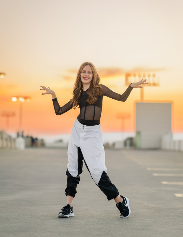 hip hop dancer girl wiht arms up by shoulders at sunset