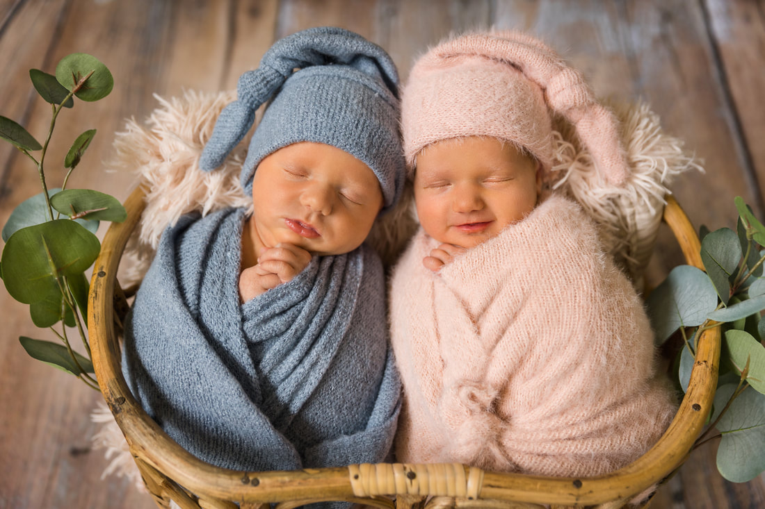 twin boy and girl newborns asleep wrapped in blankets in a wicker baket