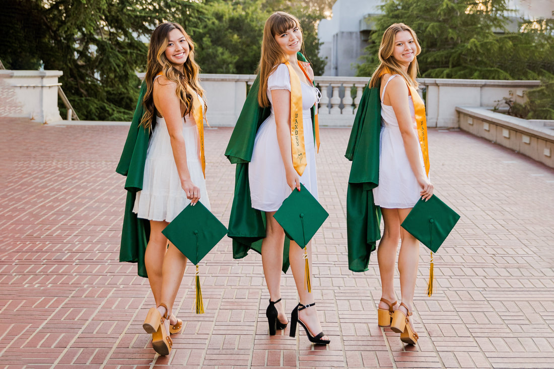 three girls wearing white dresses holding green graduation cap with gown over left shoulder