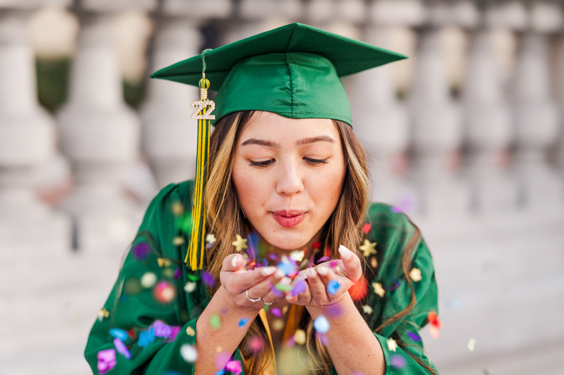 girl with green cap and gown blowing confetti