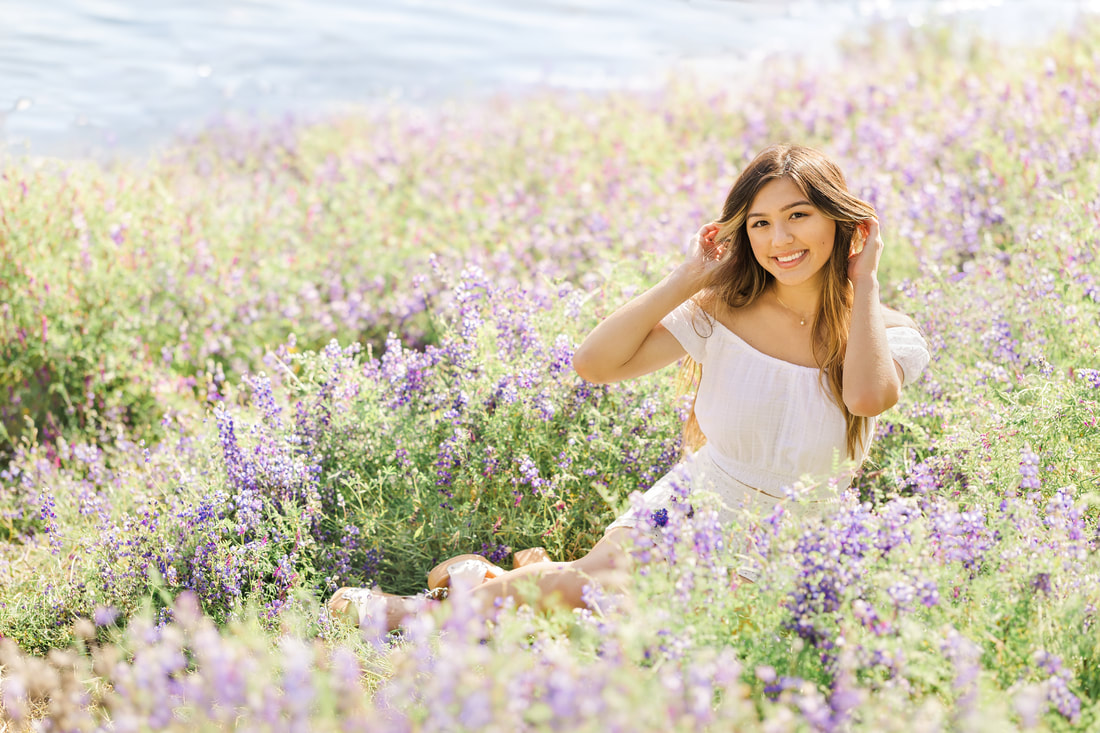 teenage girl with long brown hair and white dress sitting in purple flower field