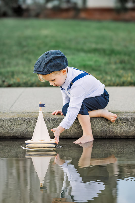 Young boy in hat pushing wooden sailboat in water