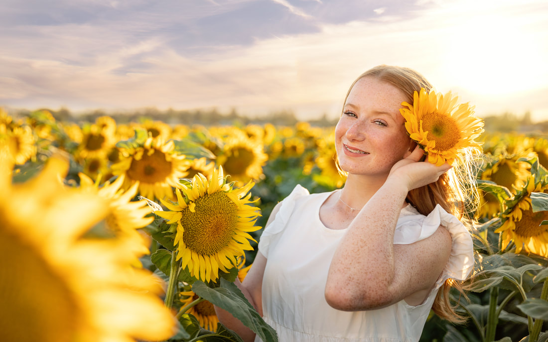 teenage girl with long red hair in a white dress in a sunflower field at sunset