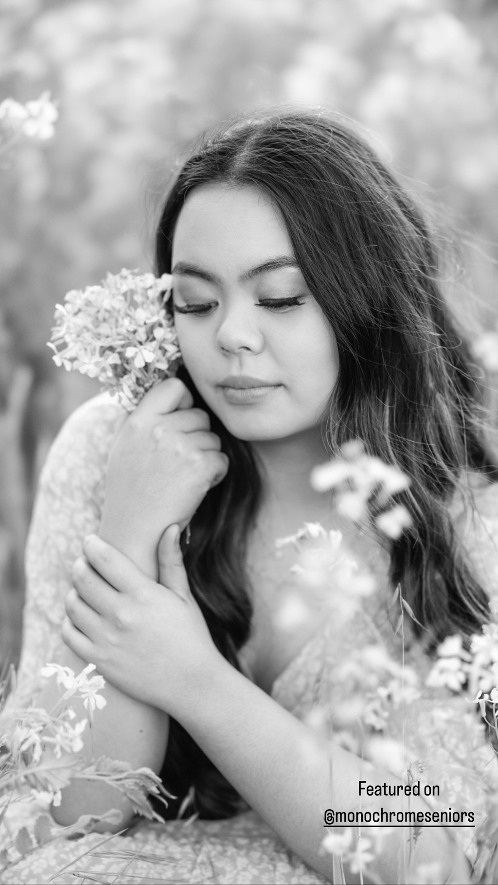 teenage girl with long dark hair holding flowers by face with eyes closed