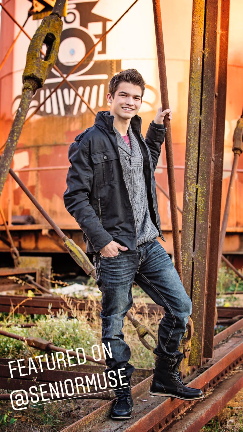 teenage boy with brown hair black jacket, blue jeans, standing on an old abandoned railroad track
