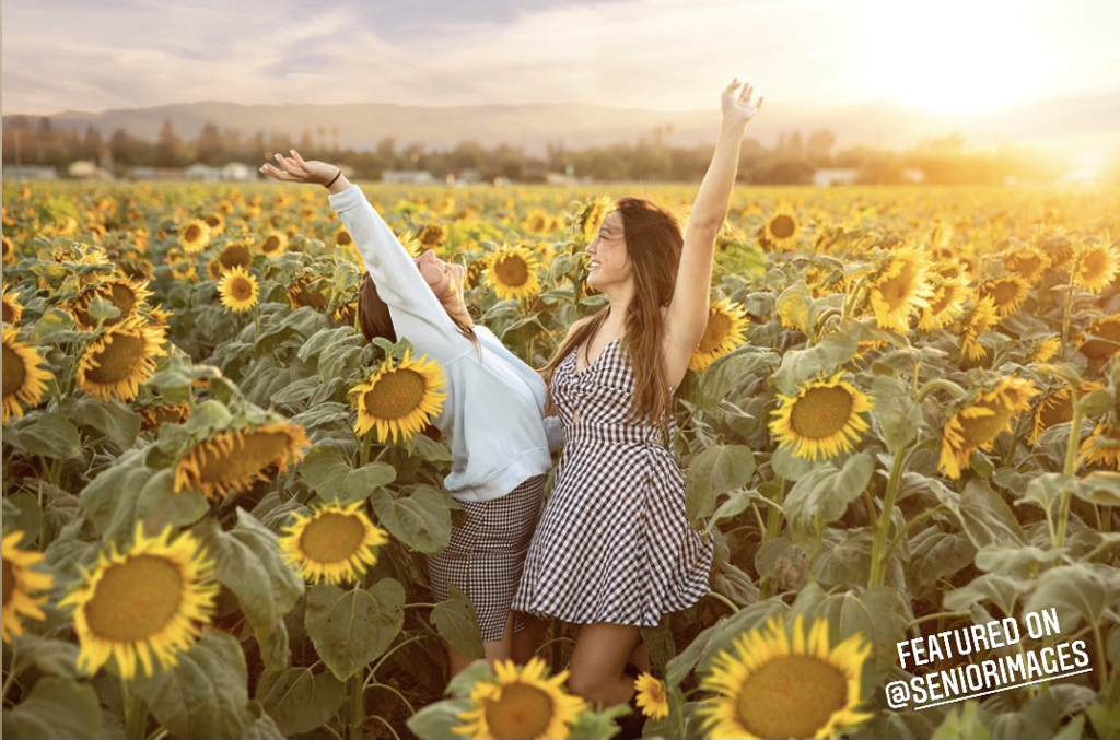 two teenage girls in sunflower field at sunset with arms up