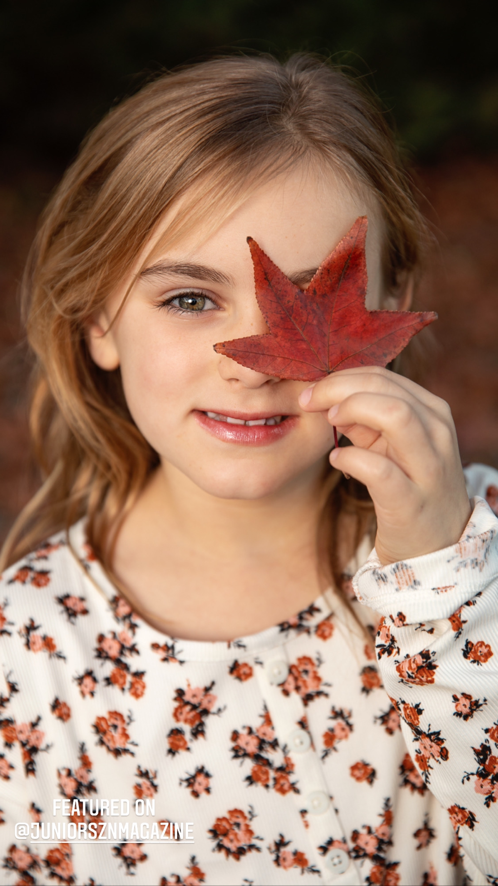 little girl holding fall red leaf in front of her eye