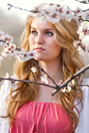 teenage girl in pink dress looking through almond blossom branches