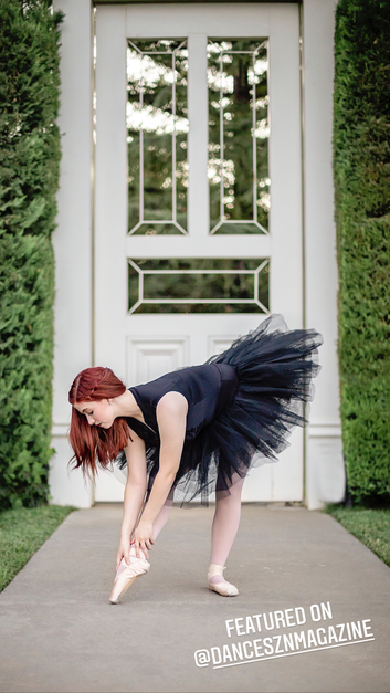 ballet dancer with red hair and black tutu putting on her slipper